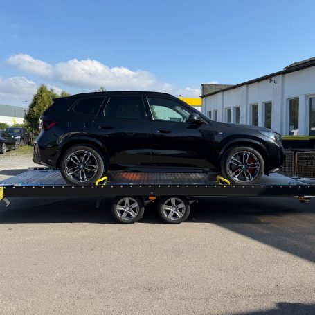Seitenansicht eines BMW iX1 in Schwarz auf dem Transportanhänger von MHX Fahrzeugtransporte