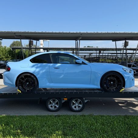 Seitenansicht des hellblauen BMW M2 auf dem Anhänger von MHX Fahrzeugtransporte