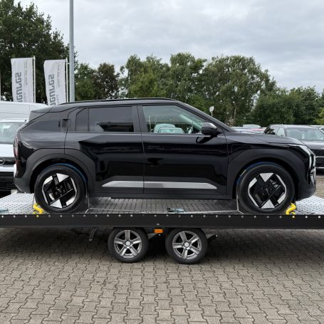 Seitenansicht eines schwarzen Kia EV3 auf dem Transportanhänger von MHX Fahrzeugtransporte