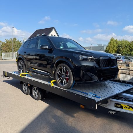 BMW iX1 in Schwarz auf dem Transportanhänger von MHX Fahrzeugtransporte aus Gütersloh